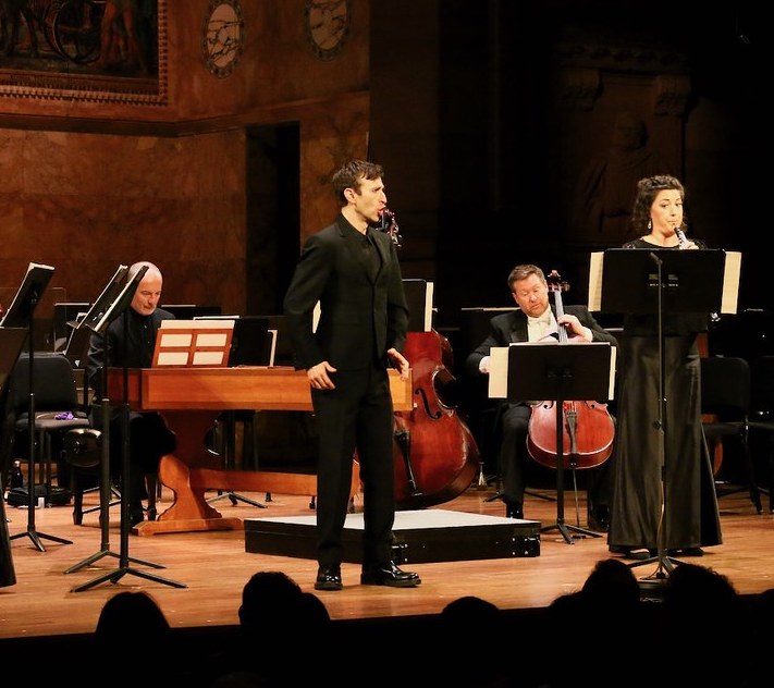 Harpsichordist, cellist, and oboist performing with an opera singer in front of an audience.