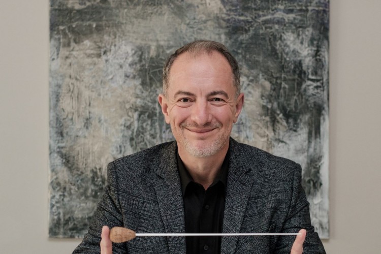 Gentleman sitting at a table holding a music conductor's baton between his hands.