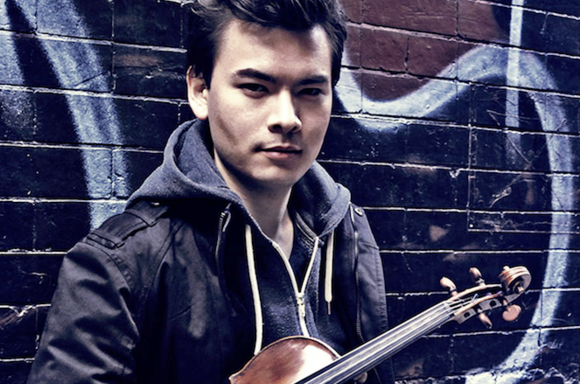 Stefan Jackiw holding a violin in front of a wall of graffiti