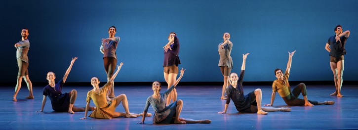 Ten Dancers, 5 standing and 5 in seated poses on stage against a blue-lit backdrop.