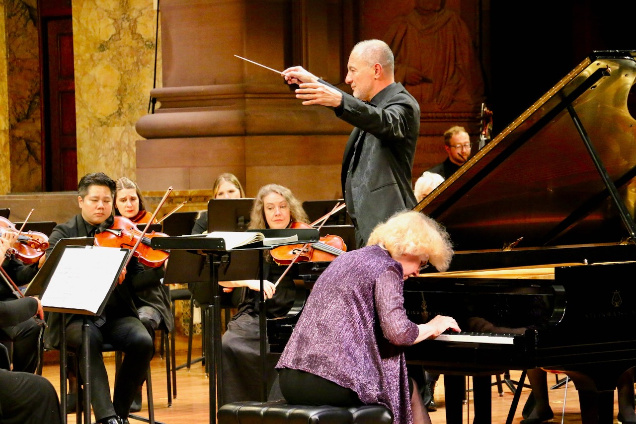 Conductor onstage with 7 string players and a solo pianist.