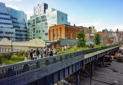 The walking path of the High Line, with the NYC skyline visible in the background. People are walking on the path.