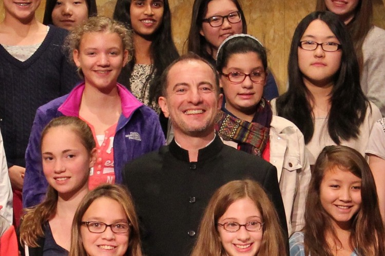 Rossen Milanov surrounded by middle school students onstage on risers.