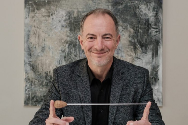 Rossen Milanov smiles at the camera and holds a conducting baton between his fingertips
