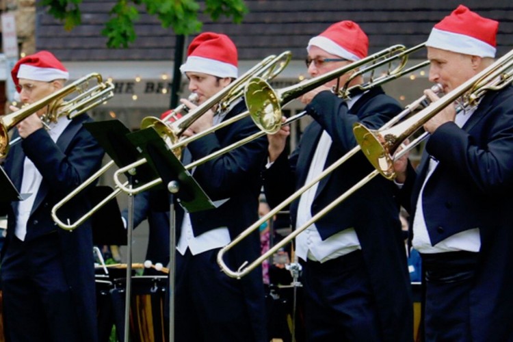 Four men standing next to each other, wearing Santa hats and playing brass instruments