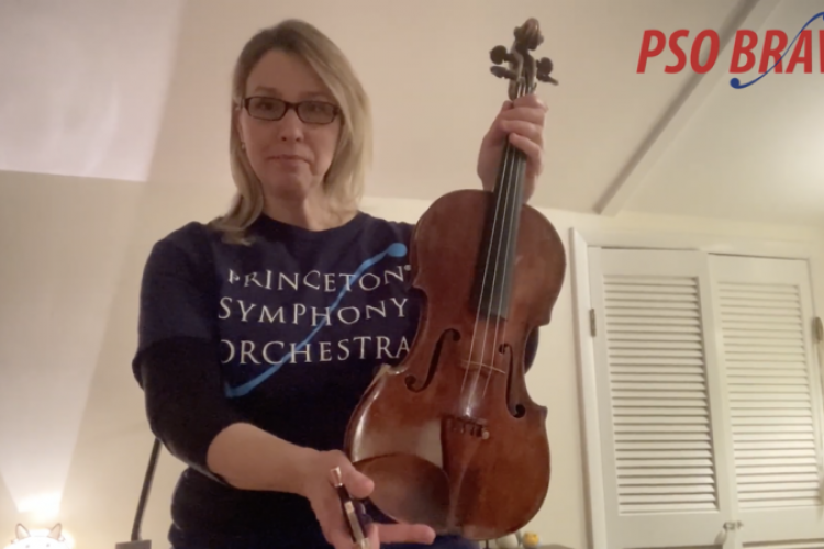 PSO Violinist and concertmaster Basia Danilow holds a violin up to the camera. The PSO BRAVO! logo is in the top right corner.