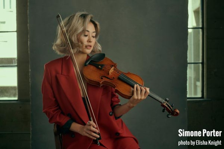 Simone Porter, seated with a violin. She has the violin and bow in position to start playing.