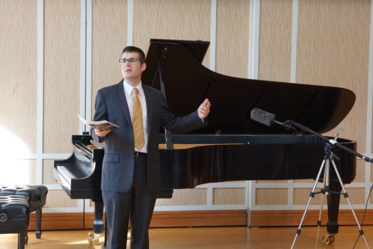 Festival Director Gregory Geehern stands in front of a piano speaking.