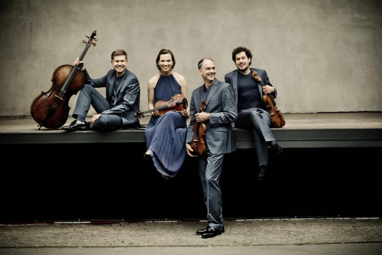 Four people sitting on the edge of a stage holding their string instruments