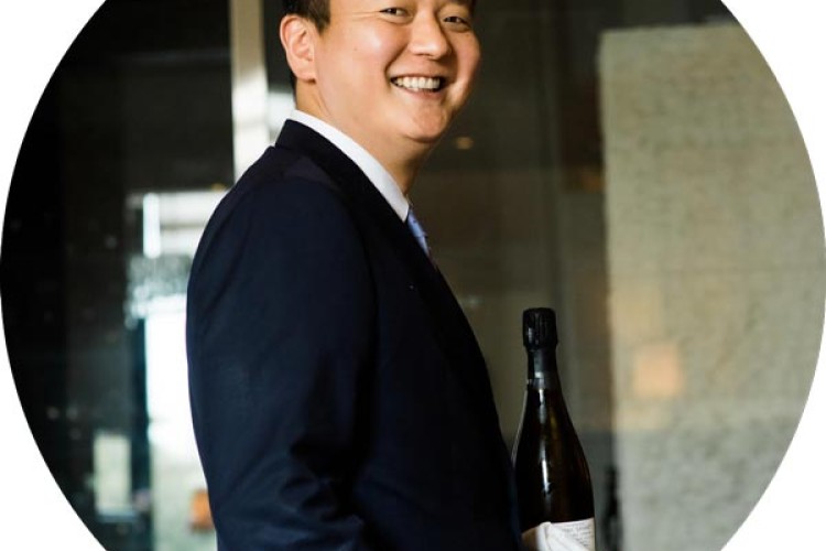 Tenor and sommelier Hak Soo Kim smiles at the camera while holding a bottle of wine