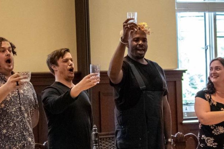 Singers Shawn Roth, Eric Delagrange, Joshua Stewart, and Ann Toomey are rehearsing. They are all standing, holding glasses raised in a toast.