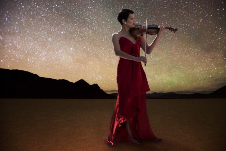 Violinist Anne Akiko Meyers playing the violin in front of a starry sky.