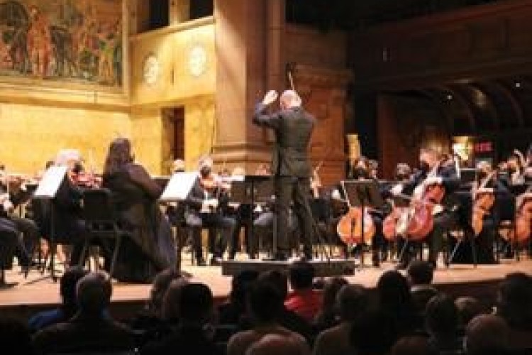 Rossen Milanov conducts the members of the Princeton Symphony Orchestra. Audience members are visible in the foreground.