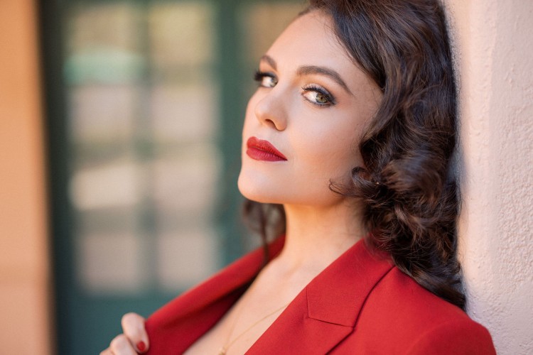 A close up of vocalist Kelly Guerra. She is wearing a red blazer and looking at the camera. 