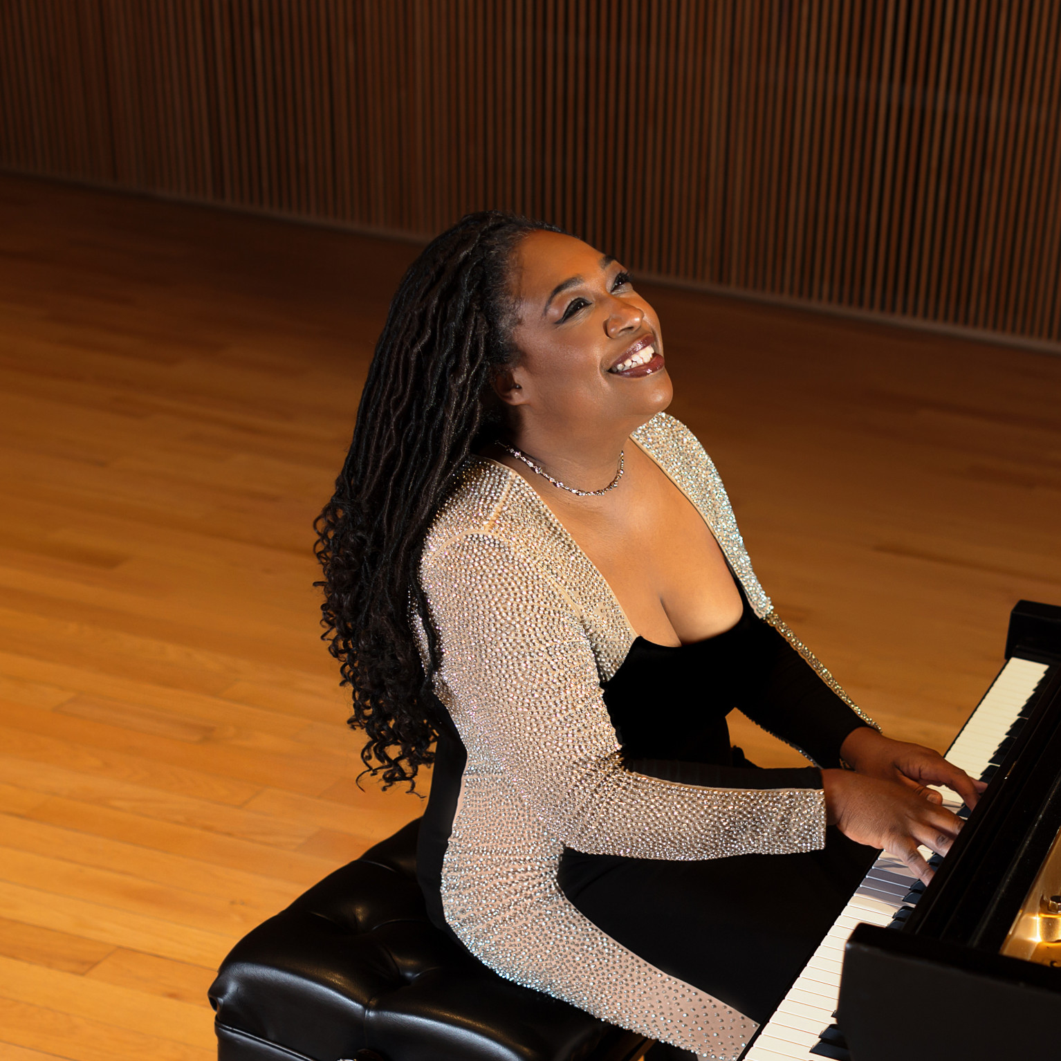 Smiling, Michelle Cann plays on a black grand piano on a wood stage..