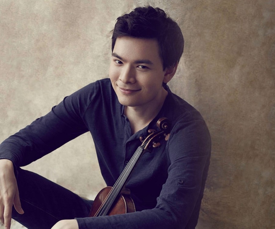 Stefan Jackiw sitting against a wall with his violin