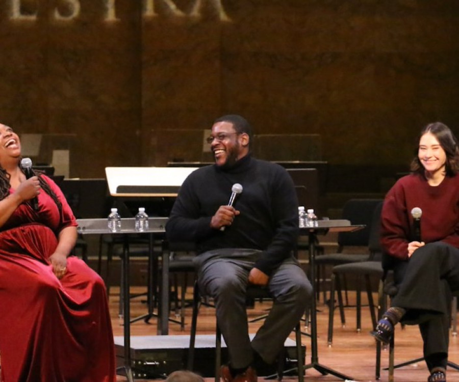 A woman throws her head back with laughter as she chats with two other people on stage during a pre-concert discussion.