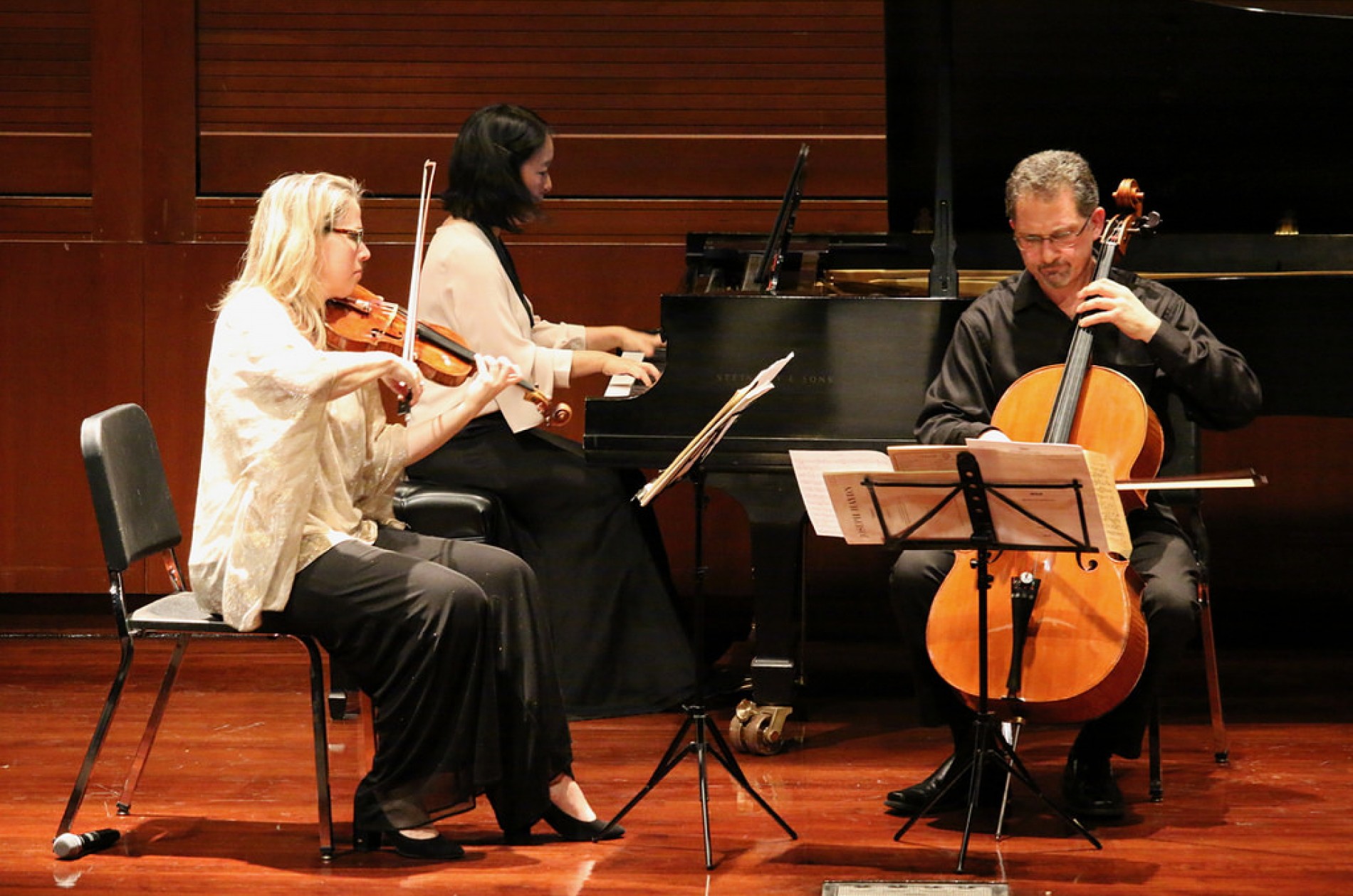 A chamber trio featuring a violinist, a pianist, and cellist performing onstage.