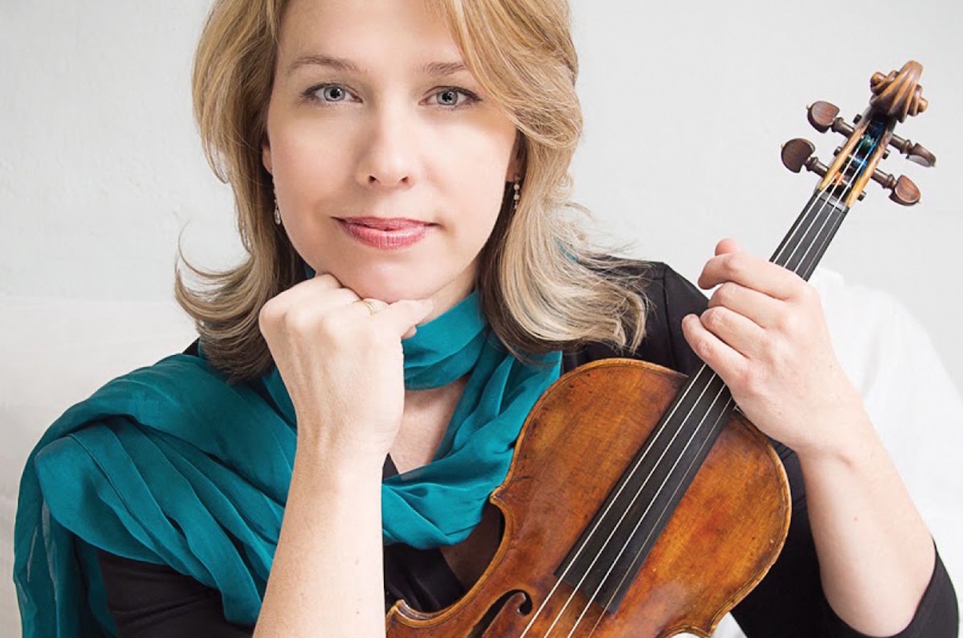Wearing a black top and teal scarf, a blond woman holds up her violin.