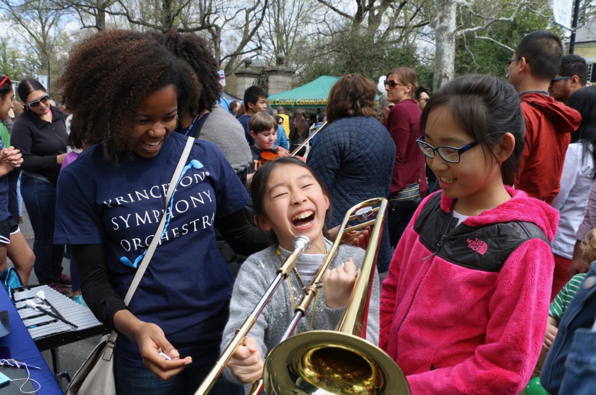 Little girl smiling holding a trombone with two girls standing next to her.